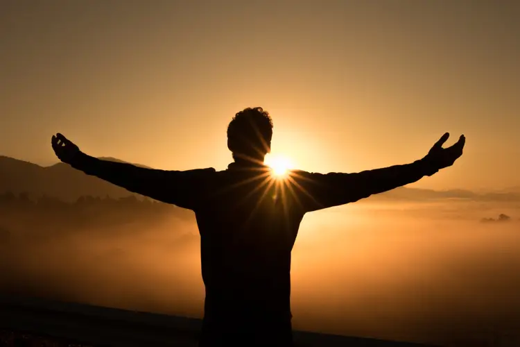 Silhouette of person with arms spread wide at sunset